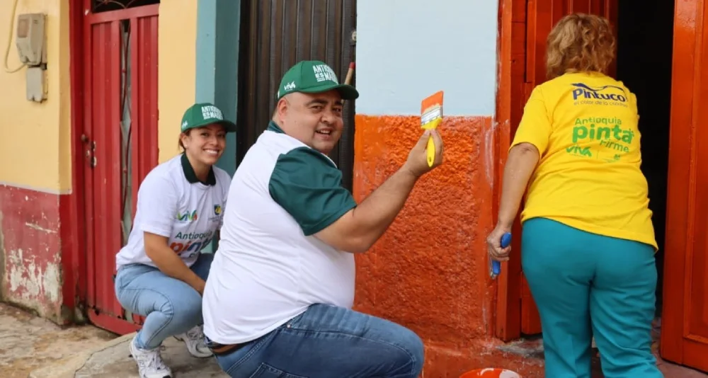 Personas con uniforme de Antioquia pinta firme, pintando fachada de una vivienda